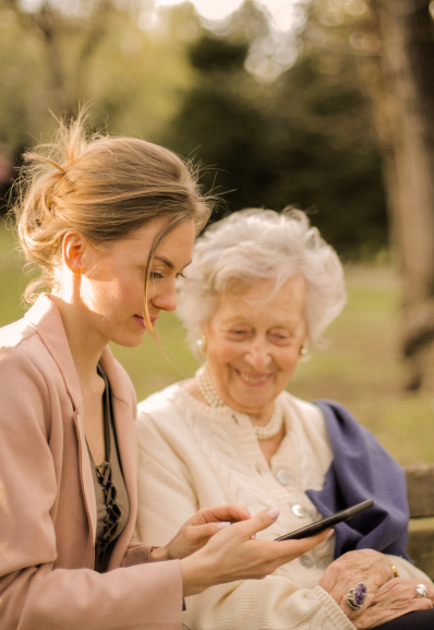 a companion helping an elderly person to use a smartphone, sitting together in a park, illustrating a moment of sharing and kindness outdoors